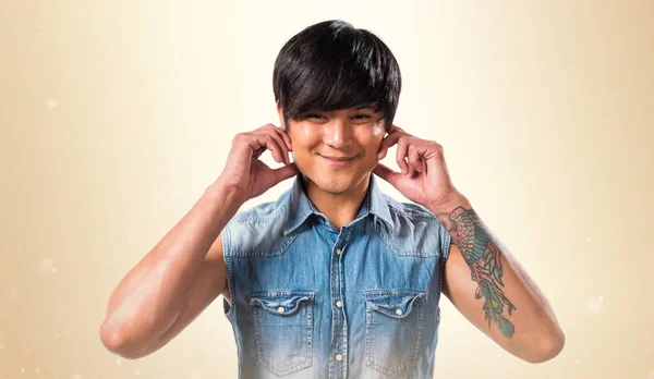 Asiático bonito homem cobrindo seus ouvidos no outro fundo — Fotografia de Stock