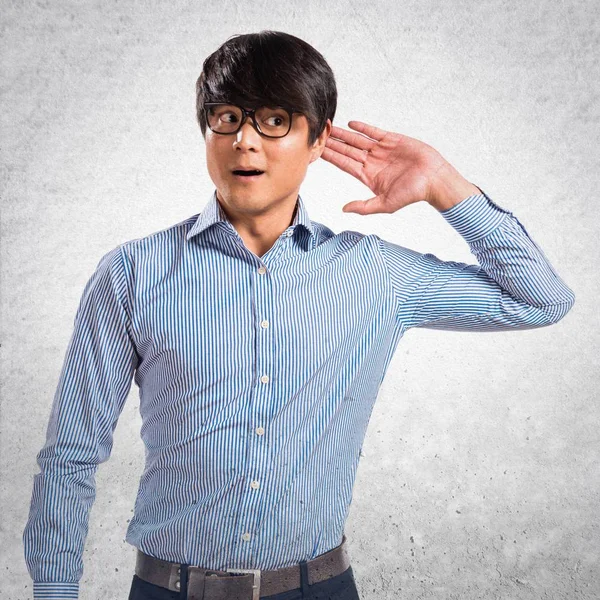 Азиатский красавчик в очках слушает что-то на текстуре — стоковое фото