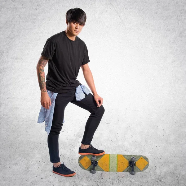 Asiático urbano hombre con skate en texturizado fondo — Foto de Stock