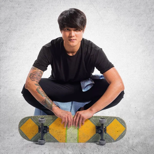 Asiático urbano hombre con skate en texturizado fondo — Foto de Stock