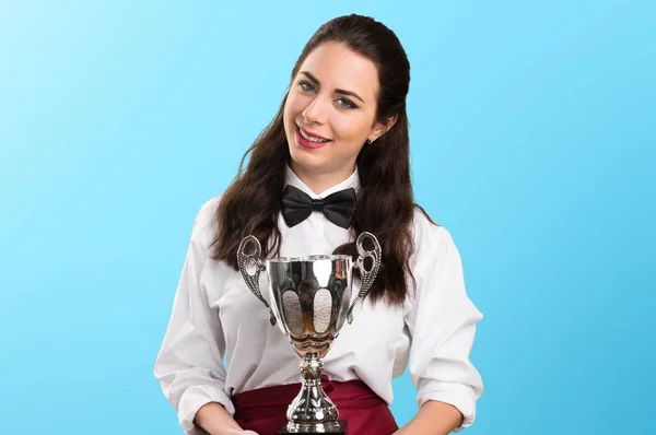 Giovane bella cameriera in possesso di un trofeo su sfondo colorato — Foto Stock