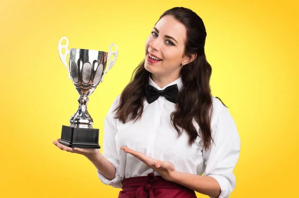 Junge schöne Kellnerin hält eine Trophäe auf buntem Hintergrund — Stockfoto