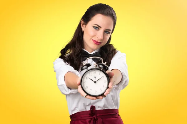 Young beautiful waitress holding vintage clock on colorful backg — Stock Photo, Image