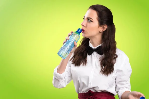 Jeune belle serveuse avec une bouteille d'eau sur fond coloré — Photo