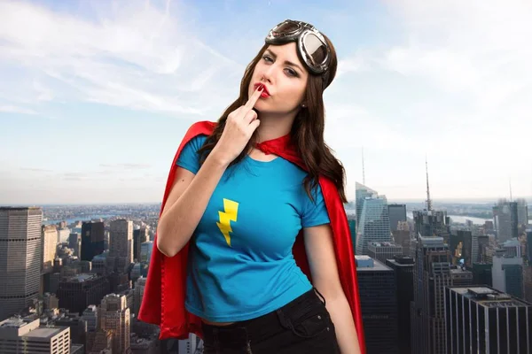 Bastante chica superhéroe haciendo gesto de cuerno con la ciudad en el fondo — Foto de Stock