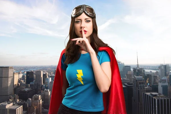 Bastante chica superhéroe haciendo gesto de silencio con la ciudad en el fondo — Foto de Stock