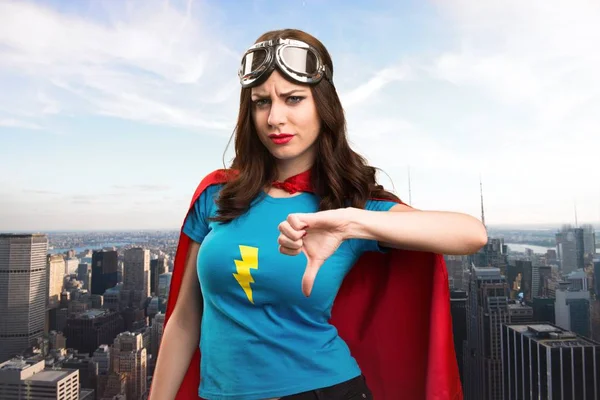 Bastante chica superhéroe haciendo mala señal con la ciudad en el fondo — Foto de Stock