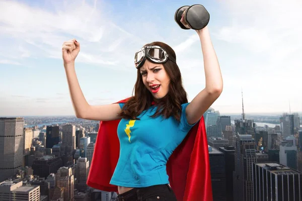 Bastante chica superhéroe haciendo levantamiento de pesas con la ciudad en el fondo — Foto de Stock