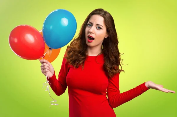 Hermosa joven sosteniendo globos y haciendo gesto sin importancia sobre fondo colorido — Foto de Stock