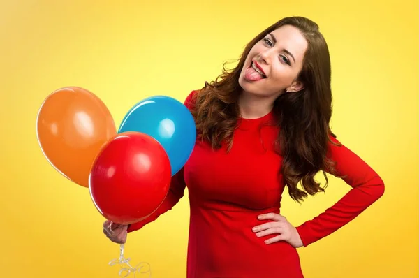 Hermosa joven sosteniendo globos y sacando su lengua sobre un fondo colorido — Foto de Stock