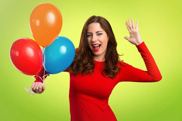 Hermosa joven sosteniendo globos y haciendo gesto sorpresa sobre fondo colorido — Foto de Stock