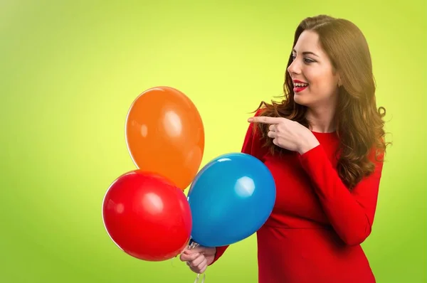 Mooi jong meisje houdt van ballonnen en wordt gewezen op de dwarskrachten op kleurrijke achtergrond — Stockfoto