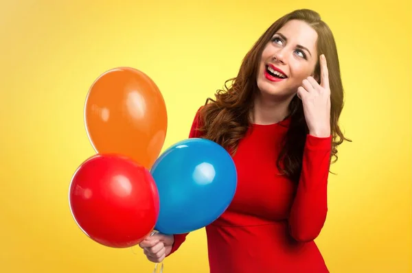 Hermosa joven sosteniendo globos y apuntando hacia arriba en el fondo colorido — Foto de Stock