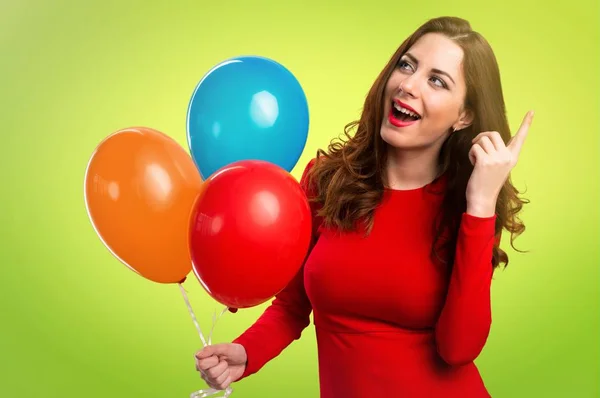Hermosa joven sosteniendo globos y pensando en fondo colorido — Foto de Stock