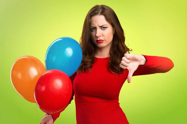 Hermosa joven sosteniendo globos y haciendo mala señal en el fondo colorido — Foto de Stock