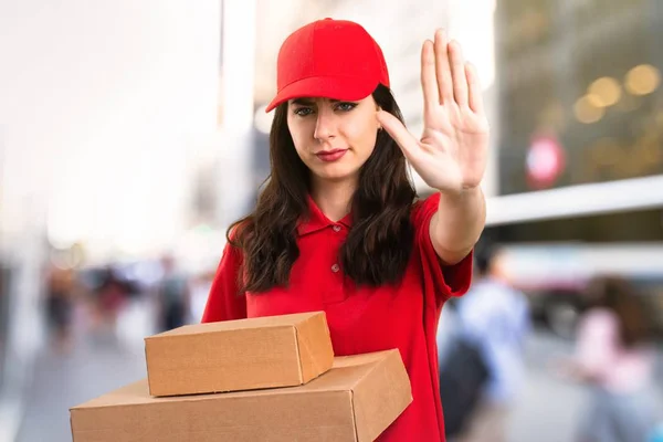 Young delivery woman making stop sign on unfocused background