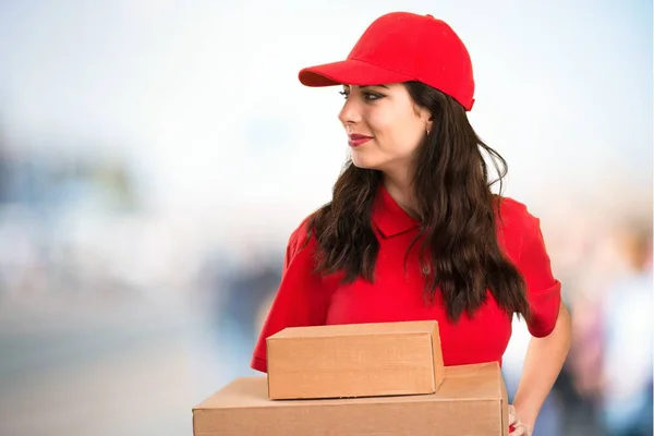 Young delivery woman looking lateral on unfocused background