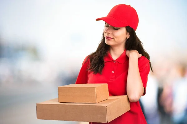 Young delivery woman with shoulder pain on unfocused background