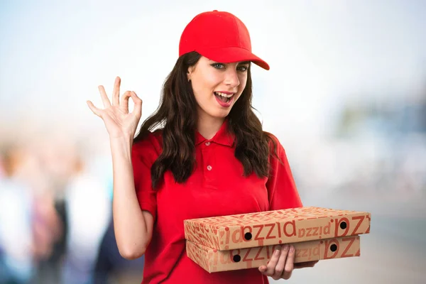 Pizza delivery woman making OK sign on unfocused background