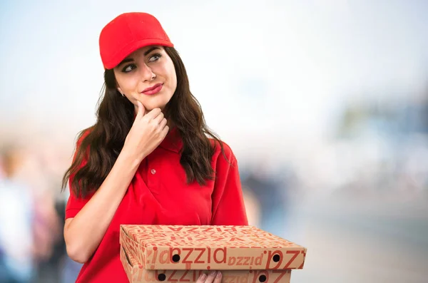 Pizza delivery woman thinking on unfocused background