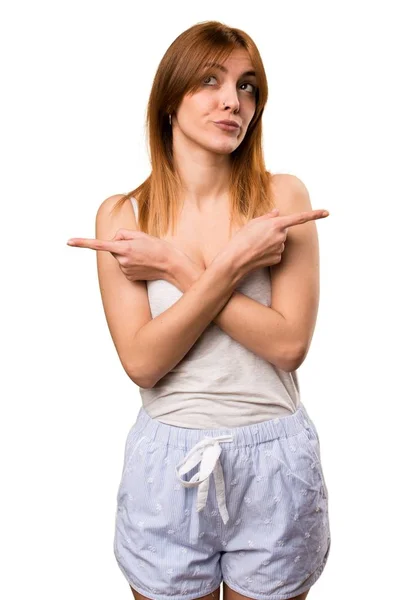 Beautiful girl in pajamas pointing to the laterals having doubts — Stock Photo, Image