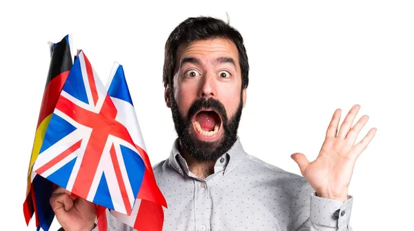 Handsome man with beard holding many flags and making surprise gesture — Stock Photo, Image