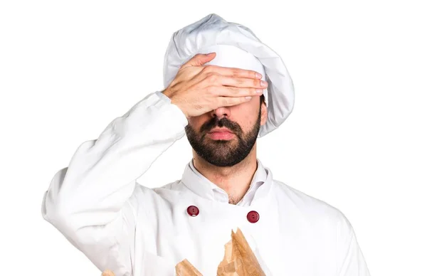 Junger Bäcker hält etwas Brot in der Hand und verdeckt seine Augen — Stockfoto