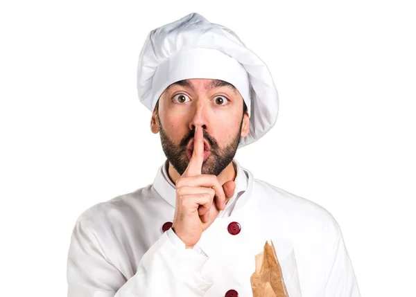 Young baker holding some bread and making silence gesture — Stock Photo, Image