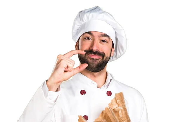 Young baker holding some bread and making tiny sign — Stock Photo, Image