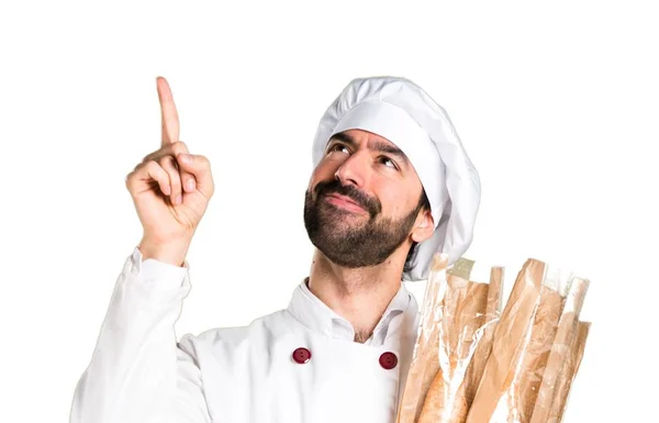 Joven panadero sosteniendo algo de pan y señalando hacia arriba — Foto de Stock