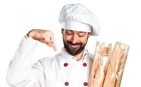 Joven panadero sosteniendo un poco de pan y apuntando hacia abajo — Foto de Stock