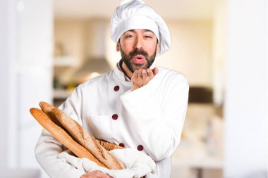 Biraz ekmek tutan ve mutfakta bir öpücük gönderme genç baker