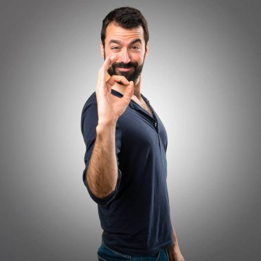 Gri arka plan üzerinde oturum Tamam yapma sakallı yakışıklı adam