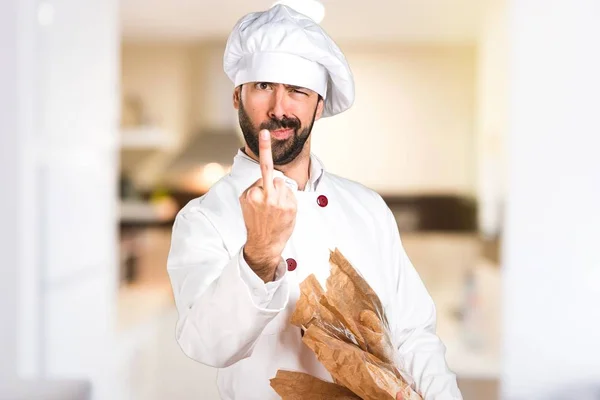 Young baker holding some bread and making horn gesture in the kitchen — Stock Photo, Image