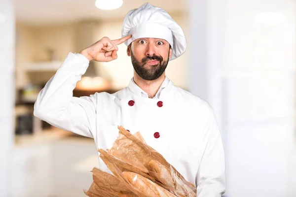 Young baker holding some bread and making crazy gesture in the kitchen