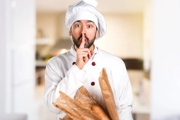 Młody piekarz trzymając niektóre chleb i podejmowania gest ciszy w kuchni — Zdjęcie stockowe
