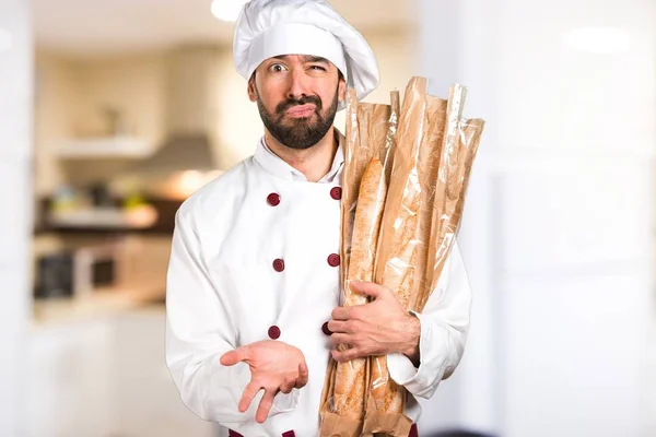 Zmęczony młody piekarz trzyma chleb w kuchni — Zdjęcie stockowe
