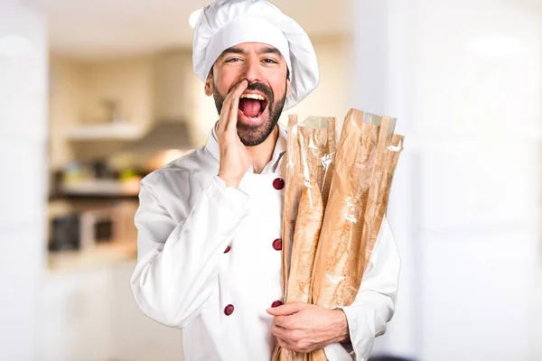 Jovem padeiro segurando um pouco de pão e gritando na cozinha — Fotografia de Stock