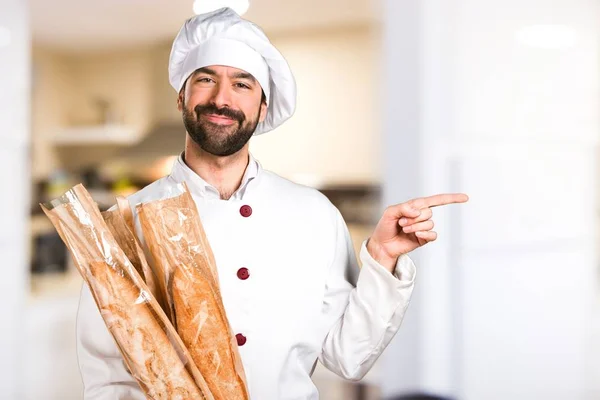 Junger Bäcker hält etwas Brot in der Hand und zeigt auf die Seite in der Küche — Stockfoto