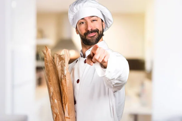 Unga bagare håller vissa bröd och pekar på framsidan i köket — Stockfoto