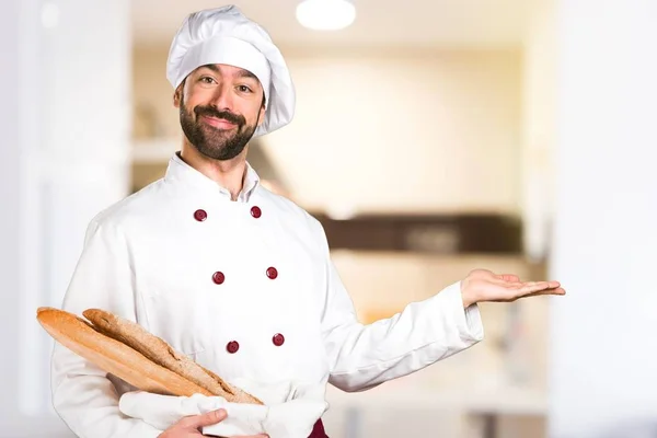 Joven panadero sosteniendo algo de pan y presentando algo en la cocina — Foto de Stock