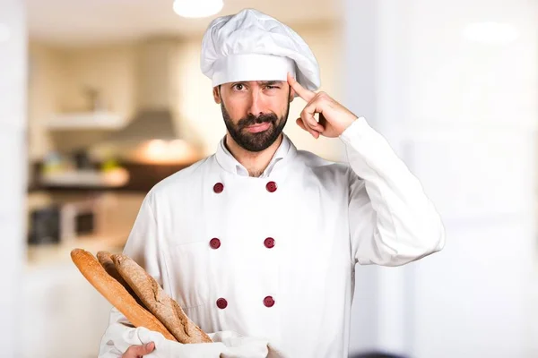 Młody piekarz trzyma chleb i myślenia w kuchni — Zdjęcie stockowe