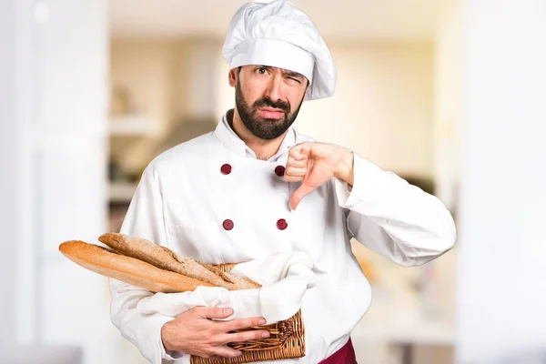 Młody piekarz trzymając niektóre chleb i podejmowania zły sygnał w kuchni — Zdjęcie stockowe