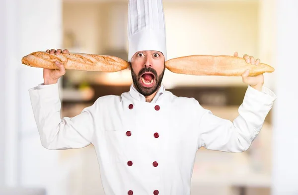 Szalony młody piekarz trzyma chleb w kuchni — Zdjęcie stockowe
