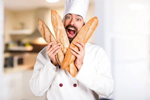 Crazy young baker holding some bread in the kitchen