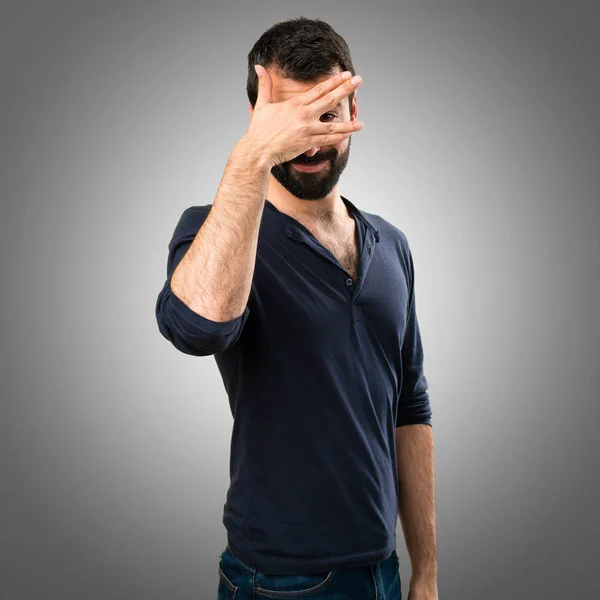 Pohledný muž s plnovousem, přikryl si oči na šedém pozadí — Stock fotografie