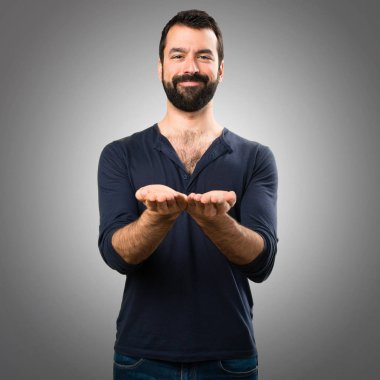 Bir şey gri arka plan üzerinde tutan sakallı yakışıklı adam