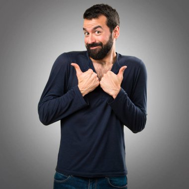 Gri arka plan üzerinde başparmak ile sakallı yakışıklı adam