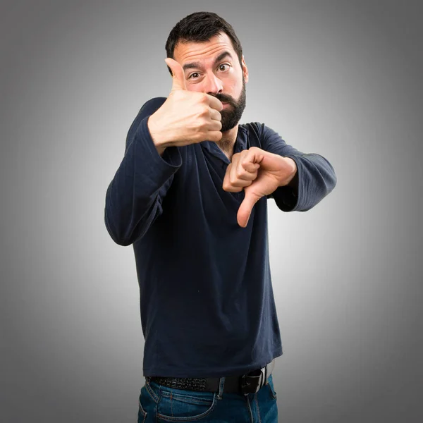 İyi-kötü işareti gri arka plan üzerinde yapma sakallı yakışıklı adam — Stok fotoğraf