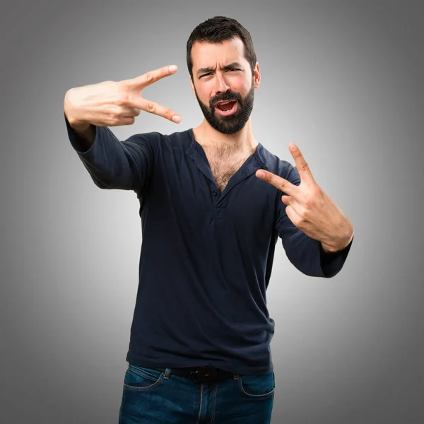 Hombre guapo con barba haciendo gesto de victoria sobre fondo gris — Foto de Stock